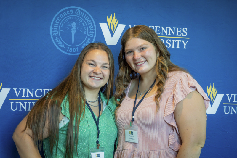 Two women smiling in front of a Vincennes University backdrop.