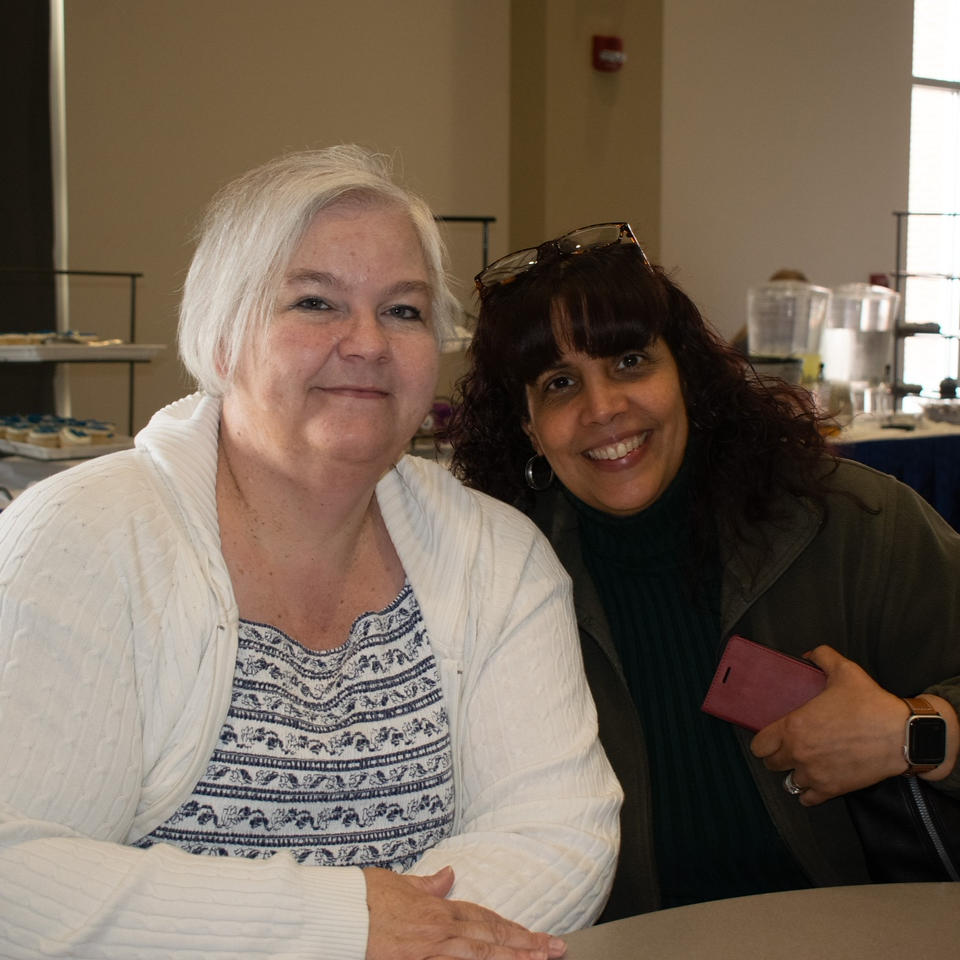 Two smiling women pose together at an indoor gathering.