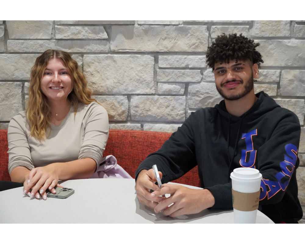 Two people sitting at a round table in front of a stone wall.