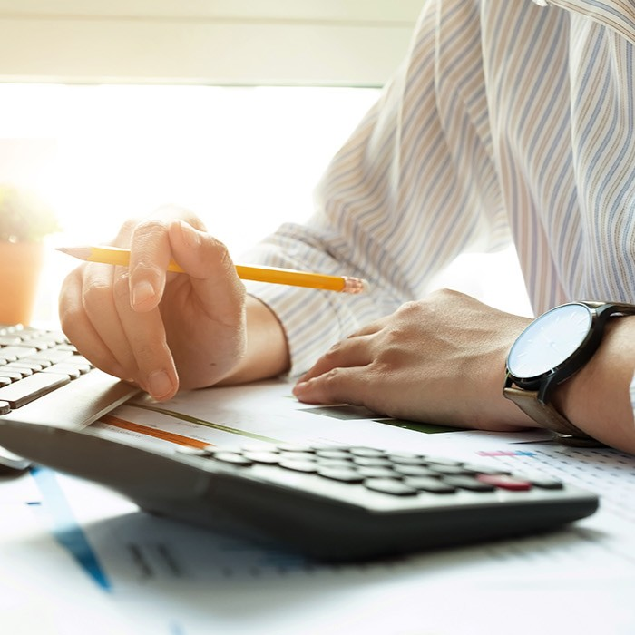 Close-up of a professional in a striped shirt using a pencil beside a laptop, papers, and calculator.