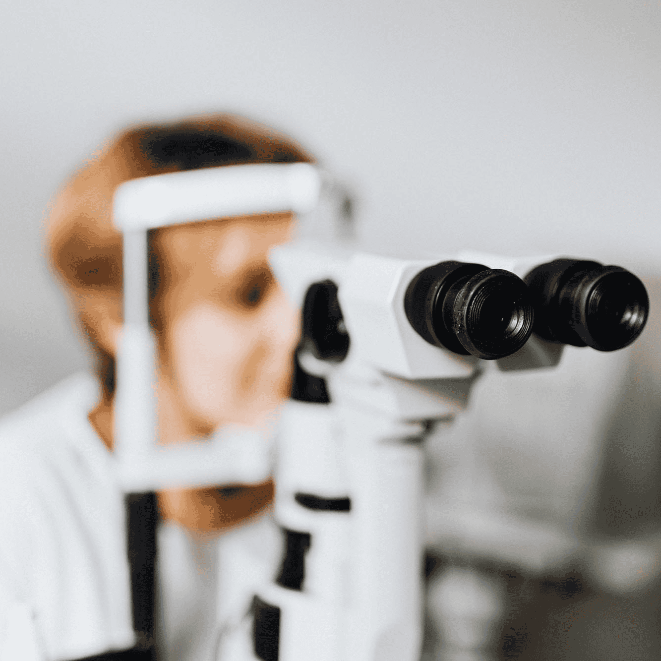 Close-up of an eye doctor using a slit lamp microscope during an eye exam, creating a clinical, focused atmosphere.