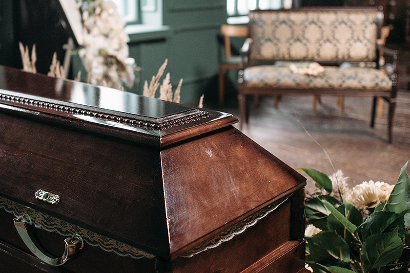 A wooden casket placed in a softly lit room, surrounded by an arrangement of colorful flowers.