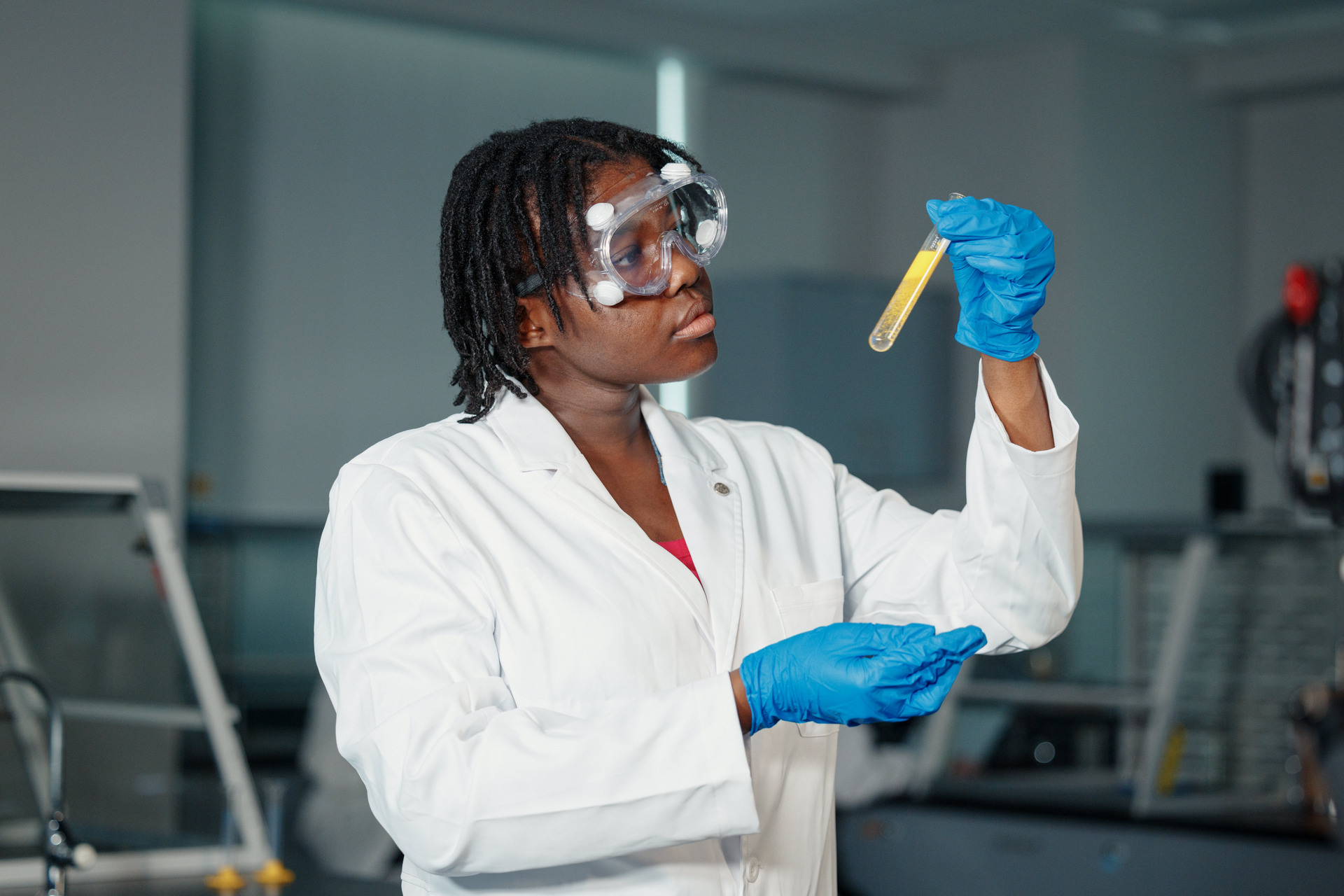 A scientist in a lab coat and goggles examines a yellow liquid in a test tube, conveying focus and curiosity, set in a laboratory.