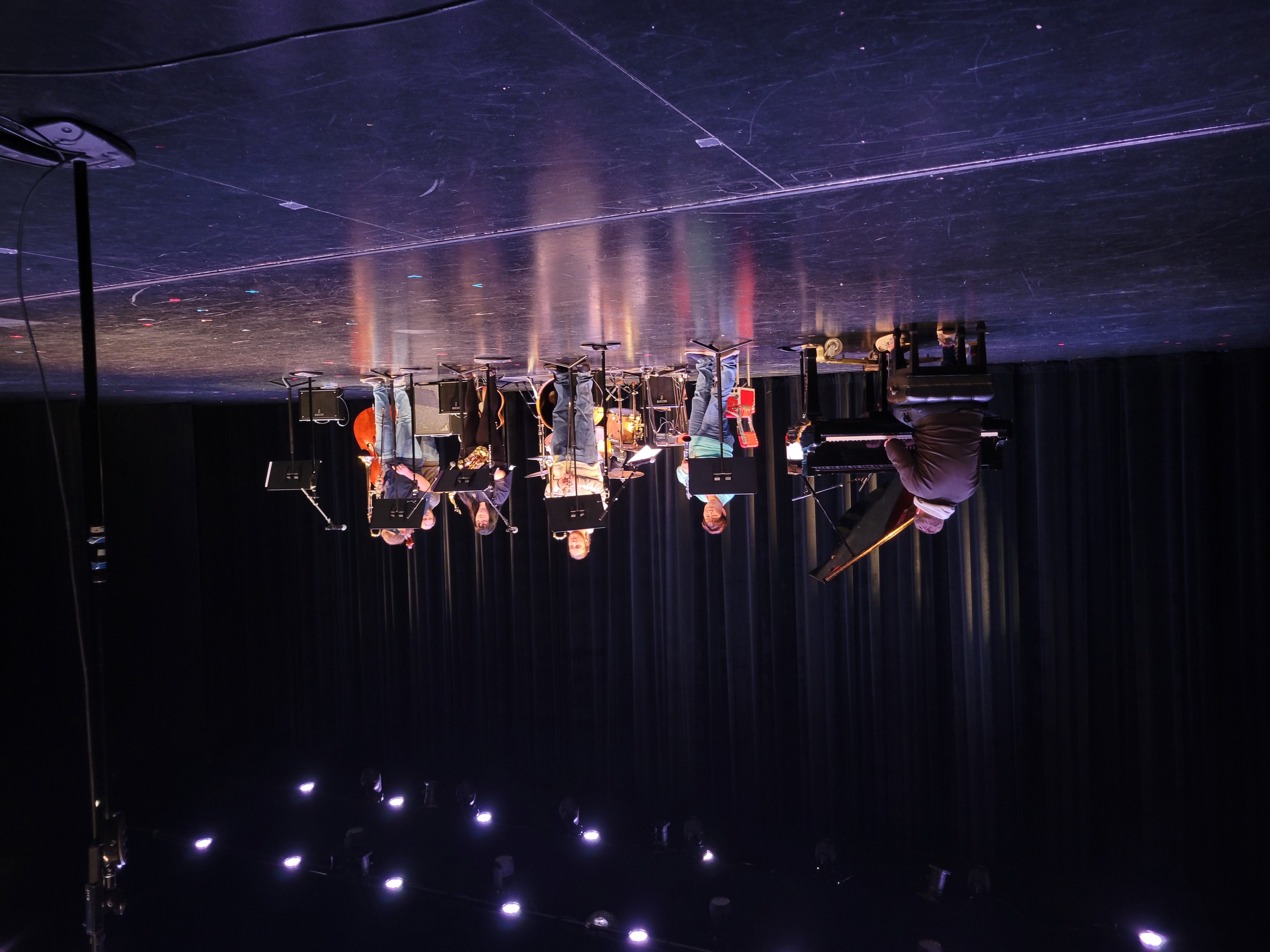 A jazz band on stage, featuring a pianist, saxophonists, and a bassist under bright stage lights. The scene conveys a lively and focused performance atmosphere.