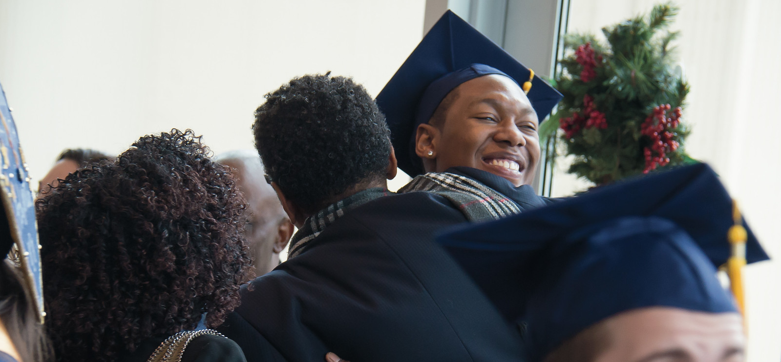 A graduate is hugging a loved one, smiling, after graduation ceremony.