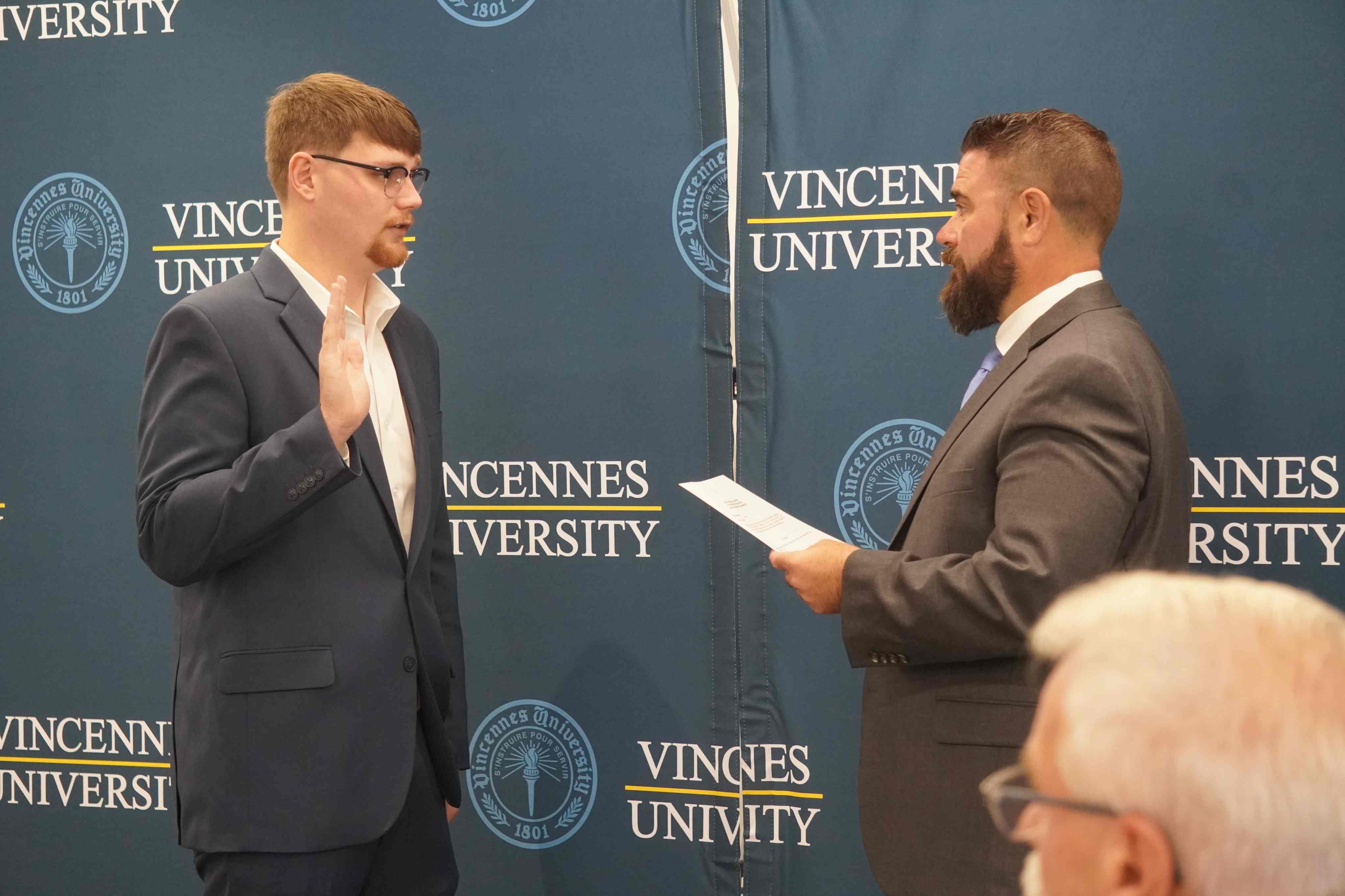 Student Trustee Cody Holmes raises his right hand while being sworn in before a Vincennes University backdrop.