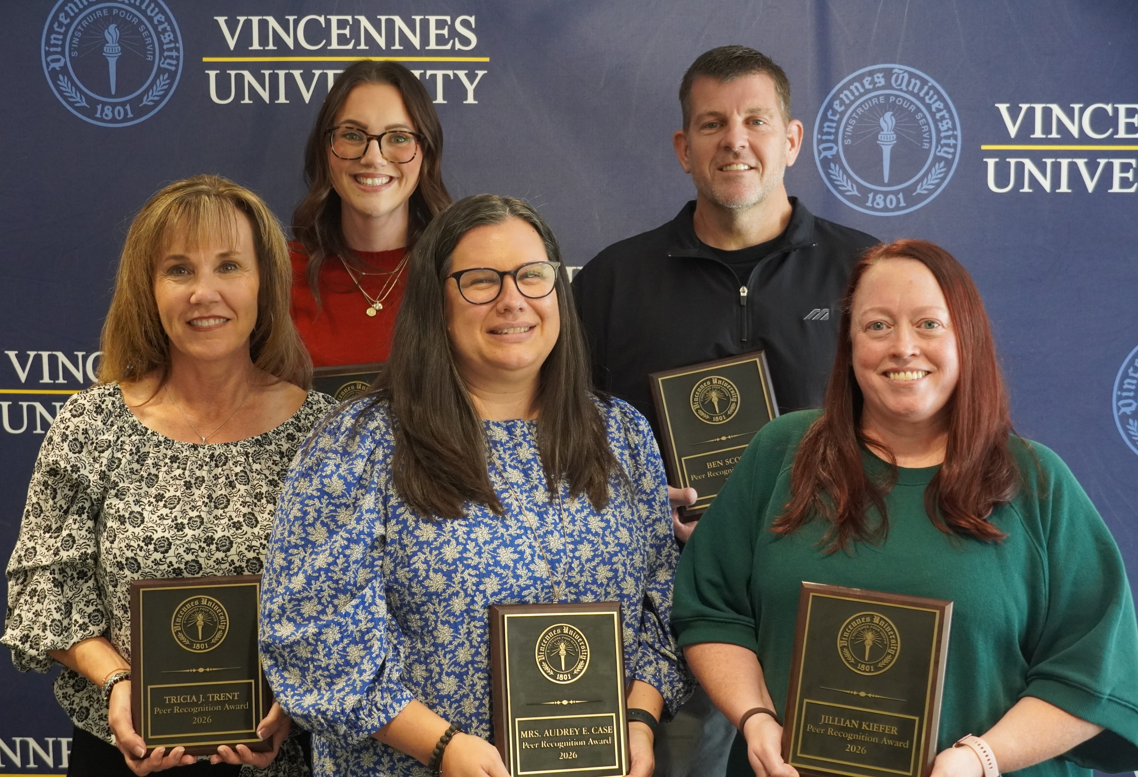 Five Vincennes University Peer Recognition Award recipients pose together holding wooden award plaques in front of a blue VU backdrop.