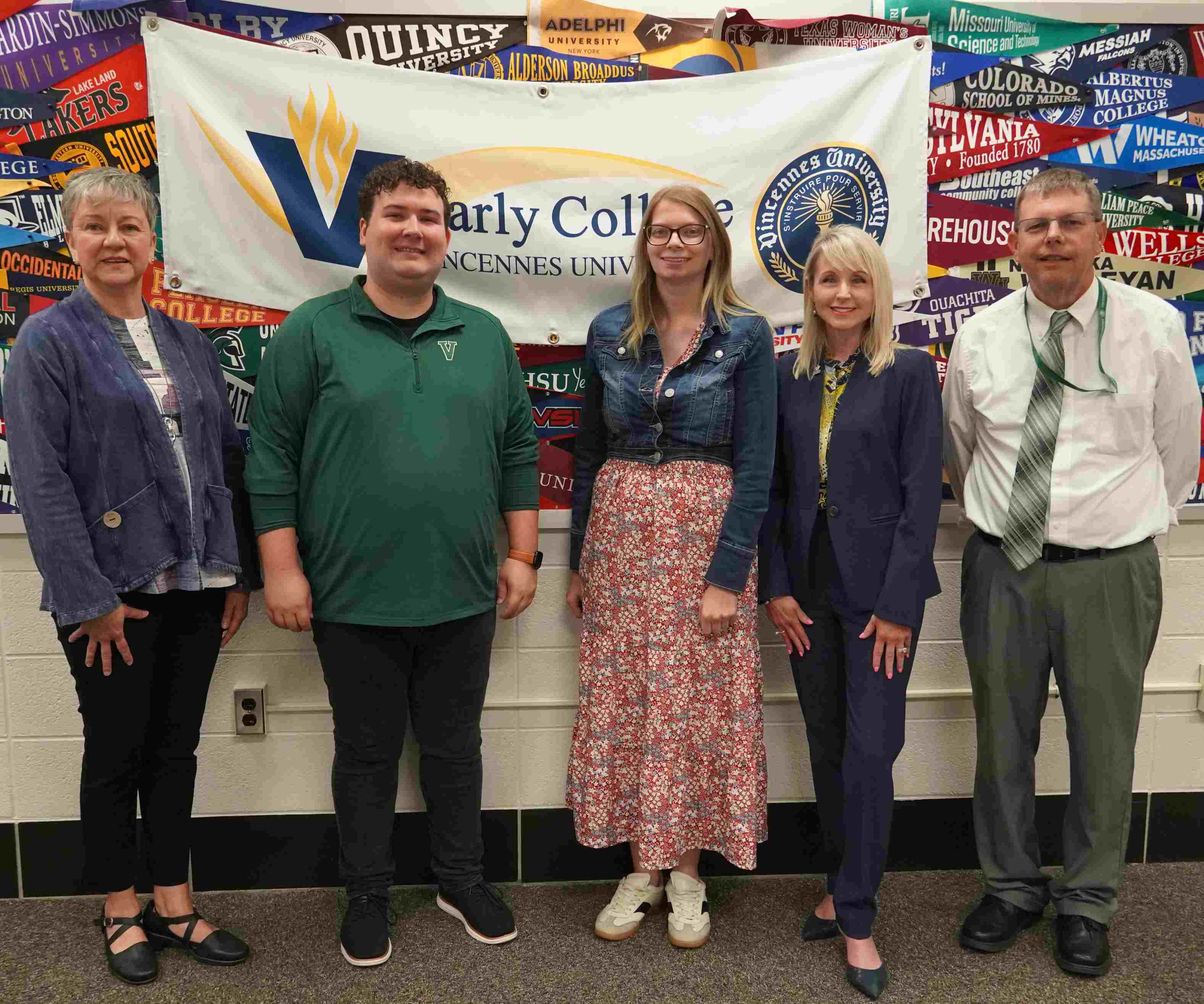 Five people pose together in front of a Vincennes University Early College banner and college pennants.