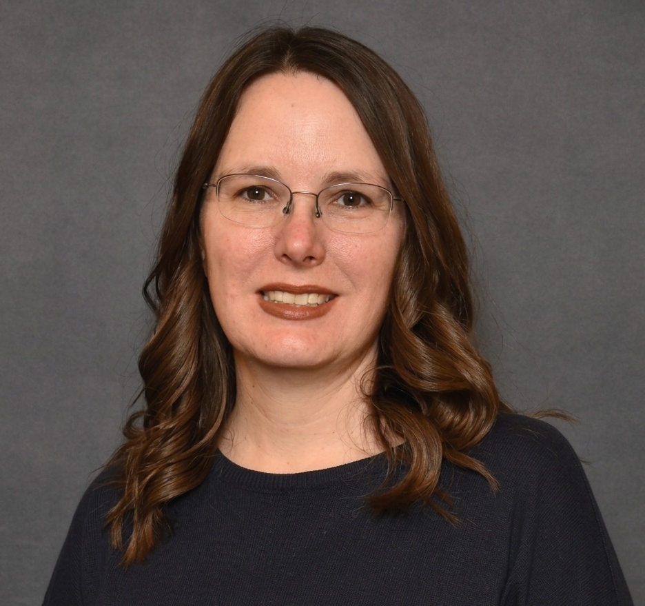 Headshot of Dr. Tammy Halter, a smiling woman with wavy brown hair and glasses wearing a dark colored shirt against a gray background.