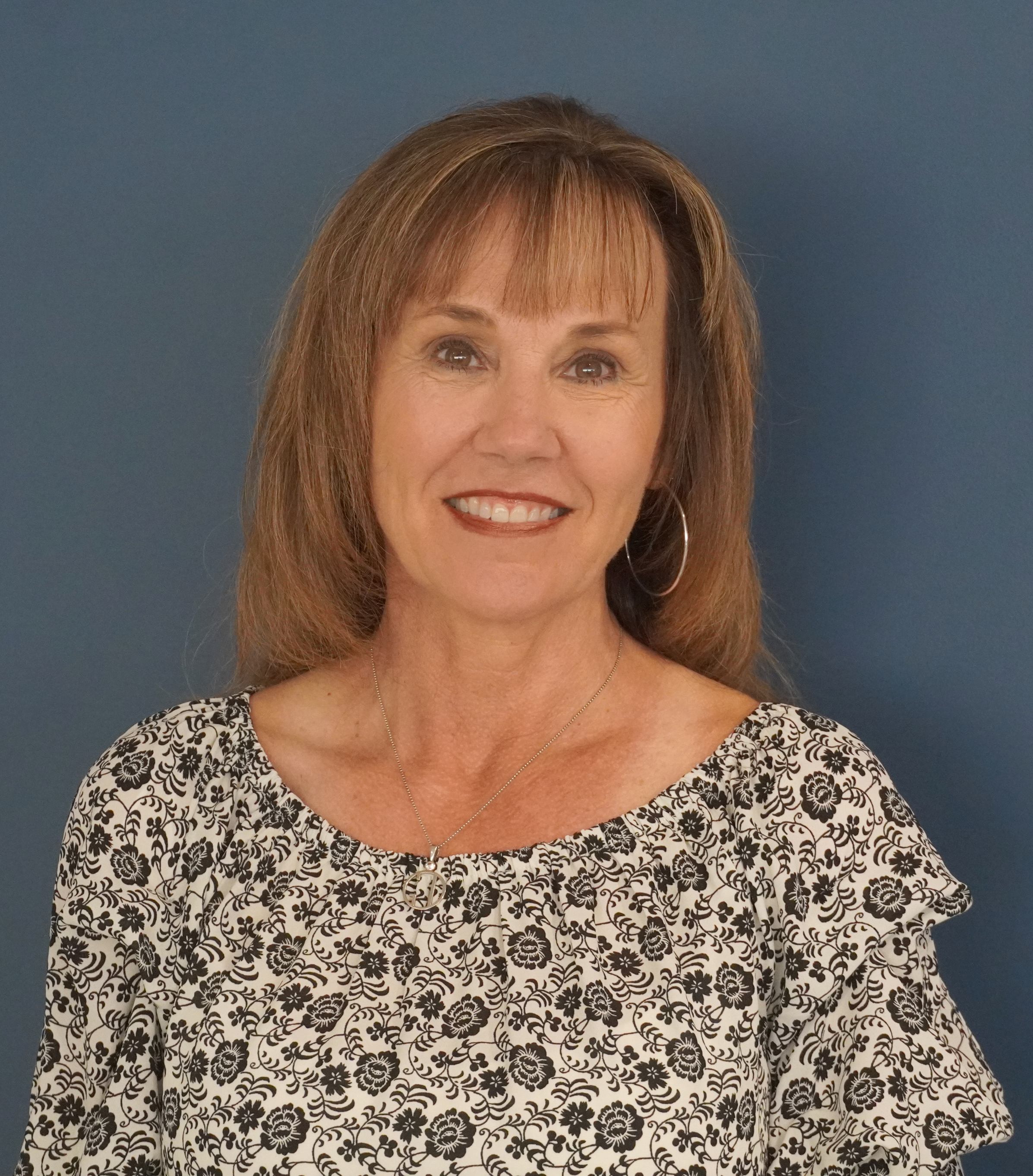 Headshot of Tricia Trent who has shoulder length hair and is wearing a white and black blouse 