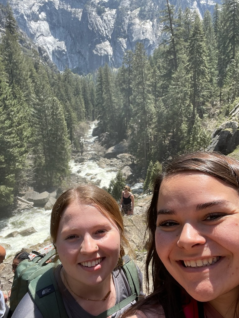 2 female VU students posing for a selfie with trees and mountains behind them.