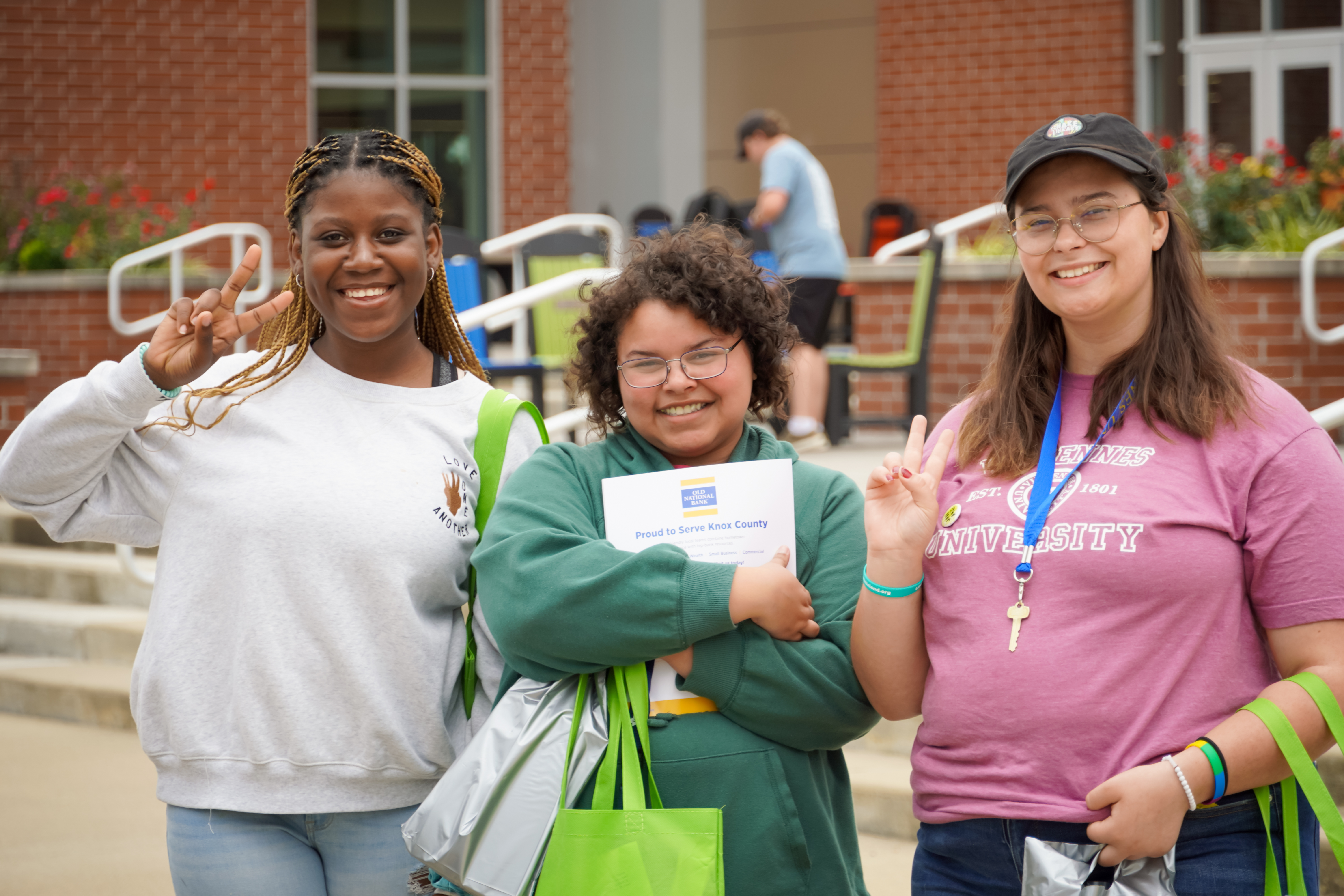 3 female students posing for a photo while smiling and 2 are flashing peace signs.