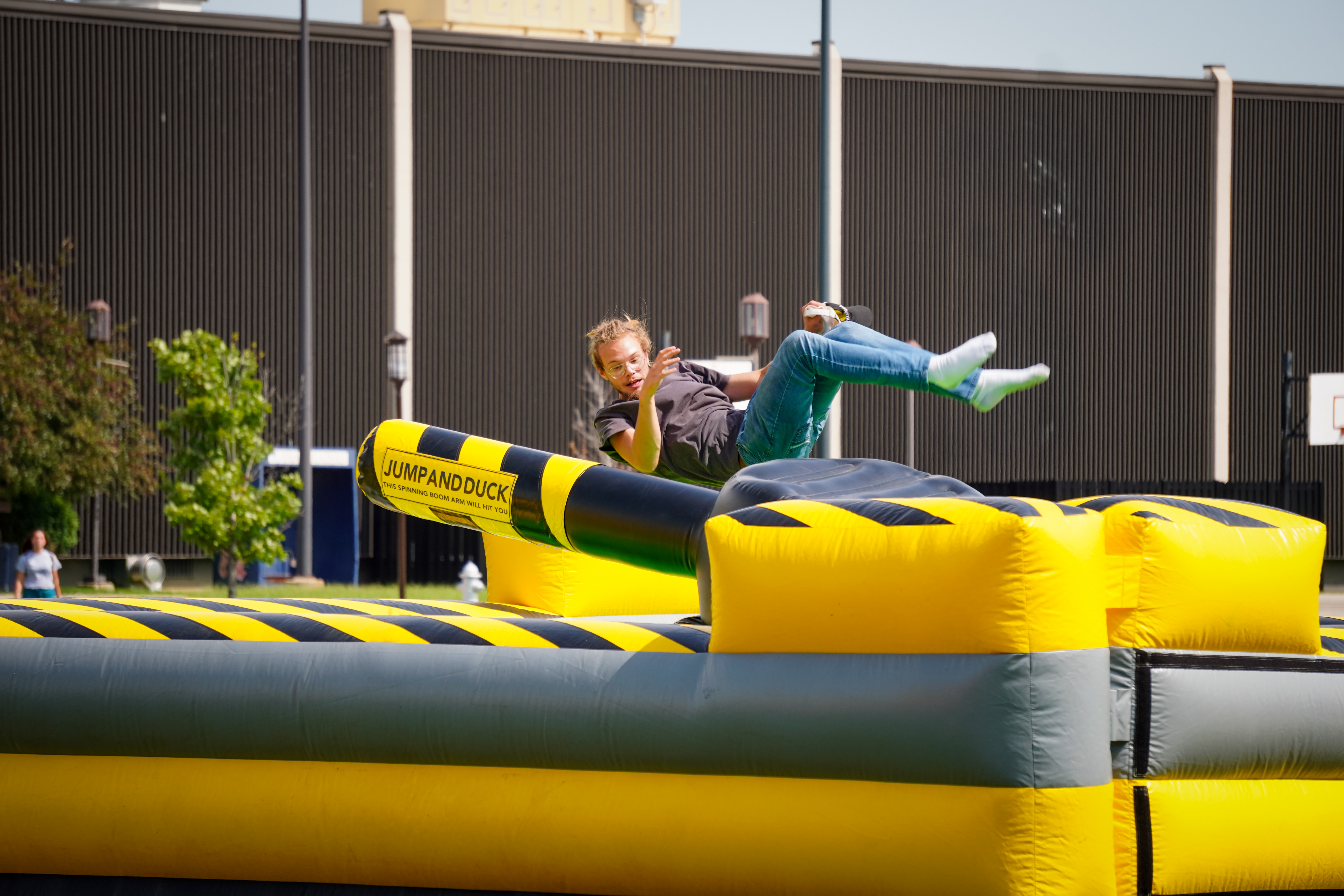 A male student is suspended in air while jumping over a rotating arm at the bounce house picnic.