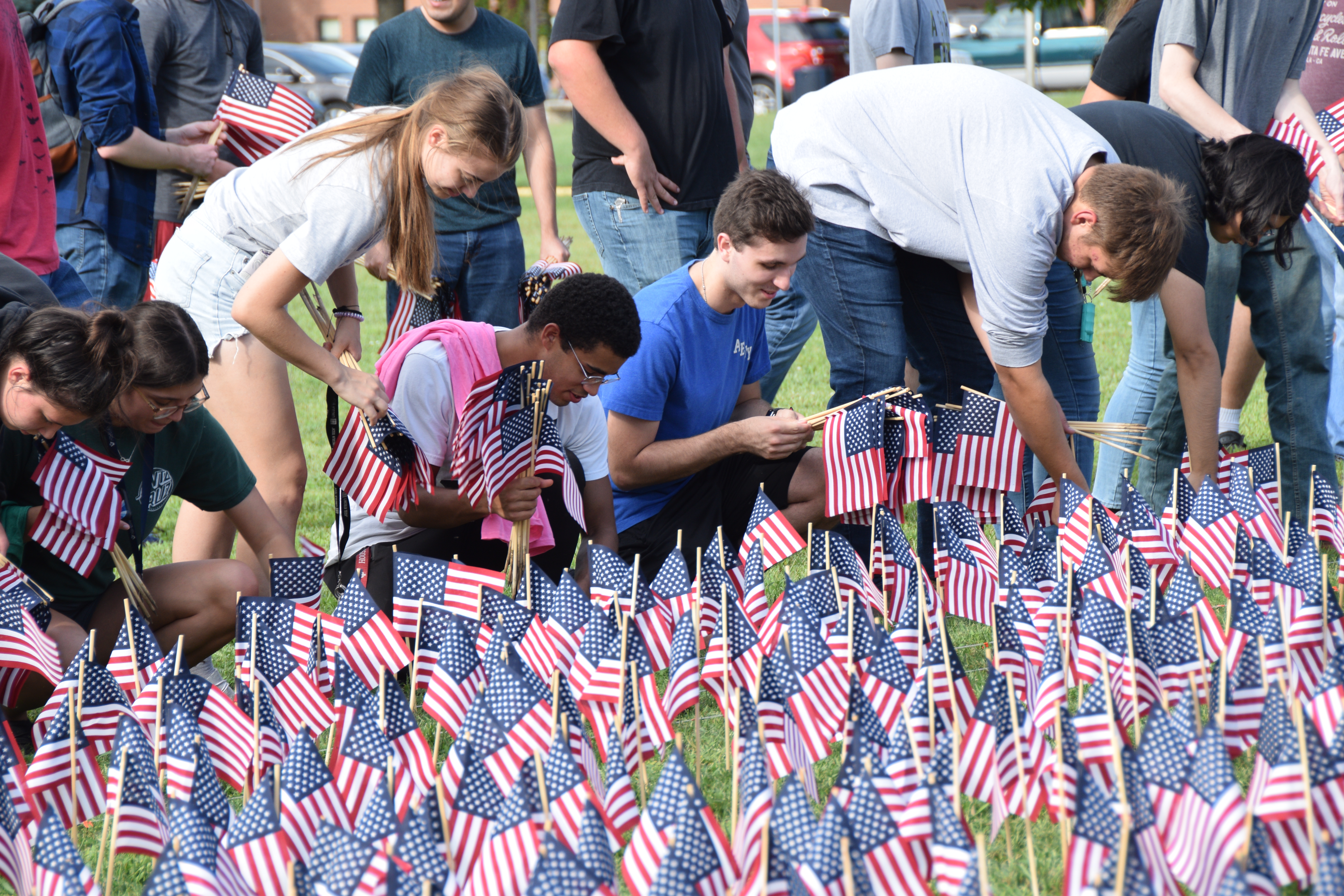 VU students holding and placing small American flags in the grass to create a 9/11 flag memorial.