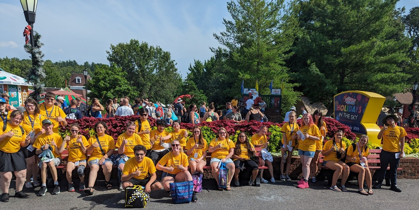JAG students, sitting and standing, wearing yellow shirts posing for a group photo at Holiday World.