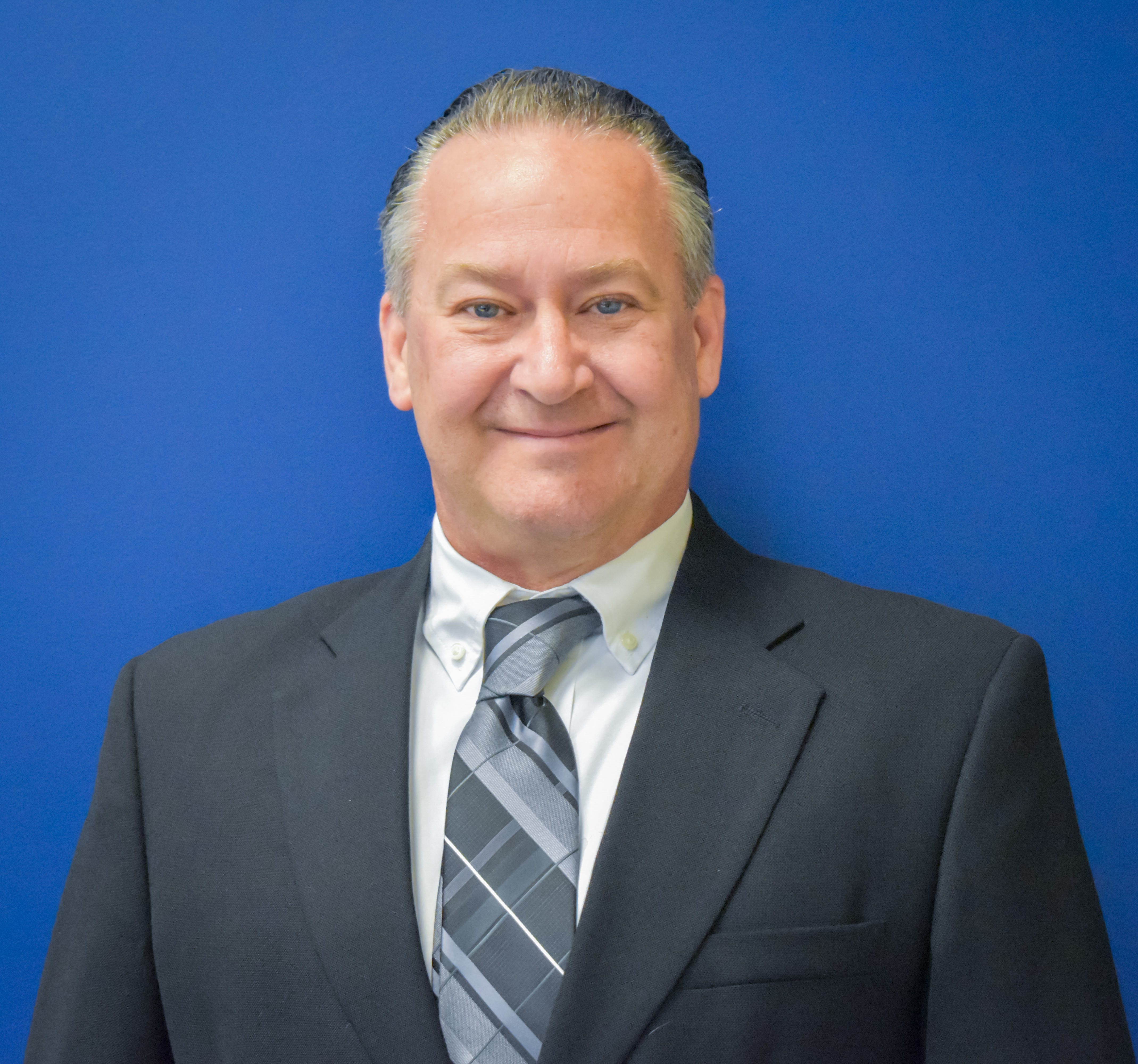 Michael Morrison wearing a suit and tie looks at camera with blue wall behind him