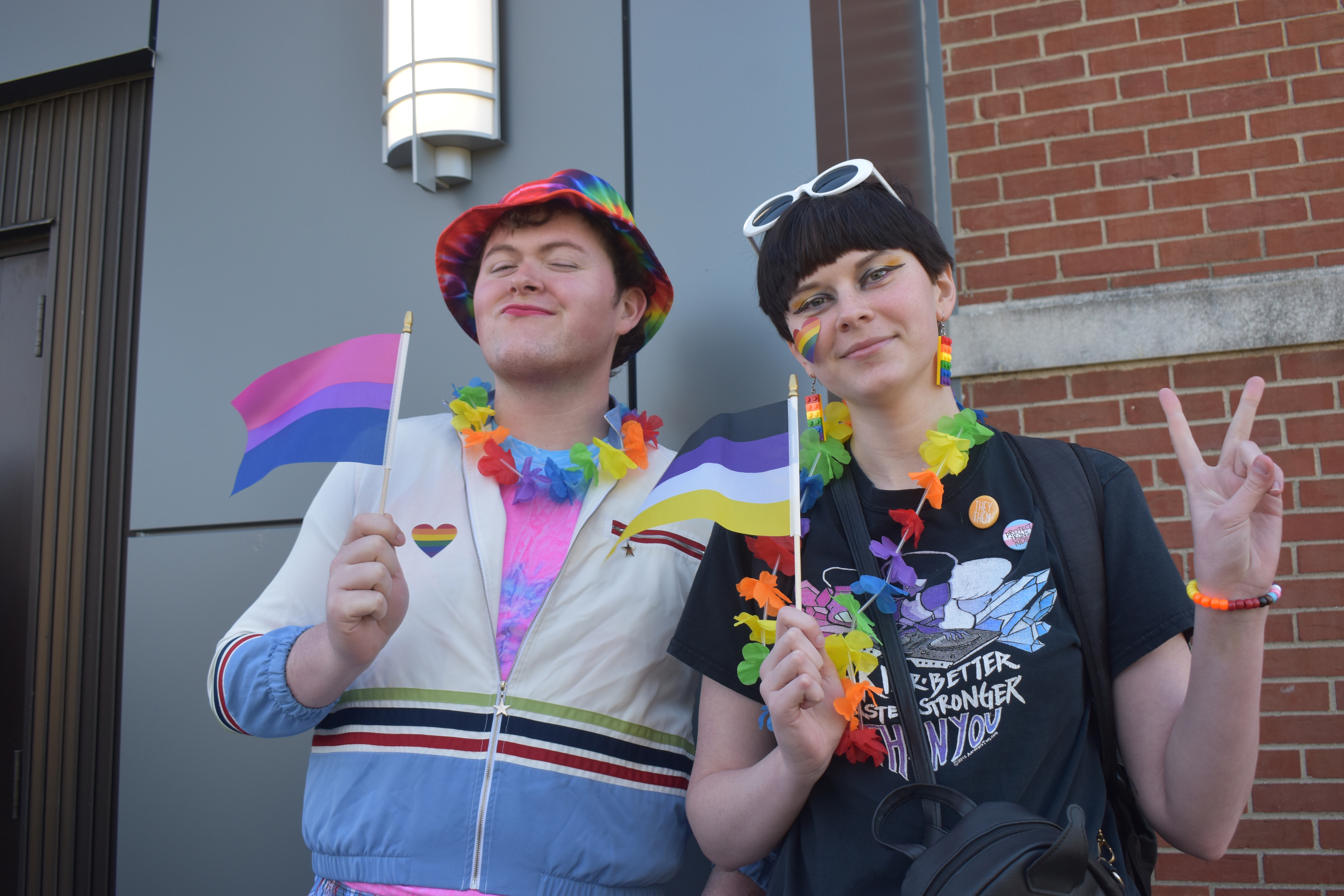 2 VU students wearing colorful clothing and accessories while holding colorful flags