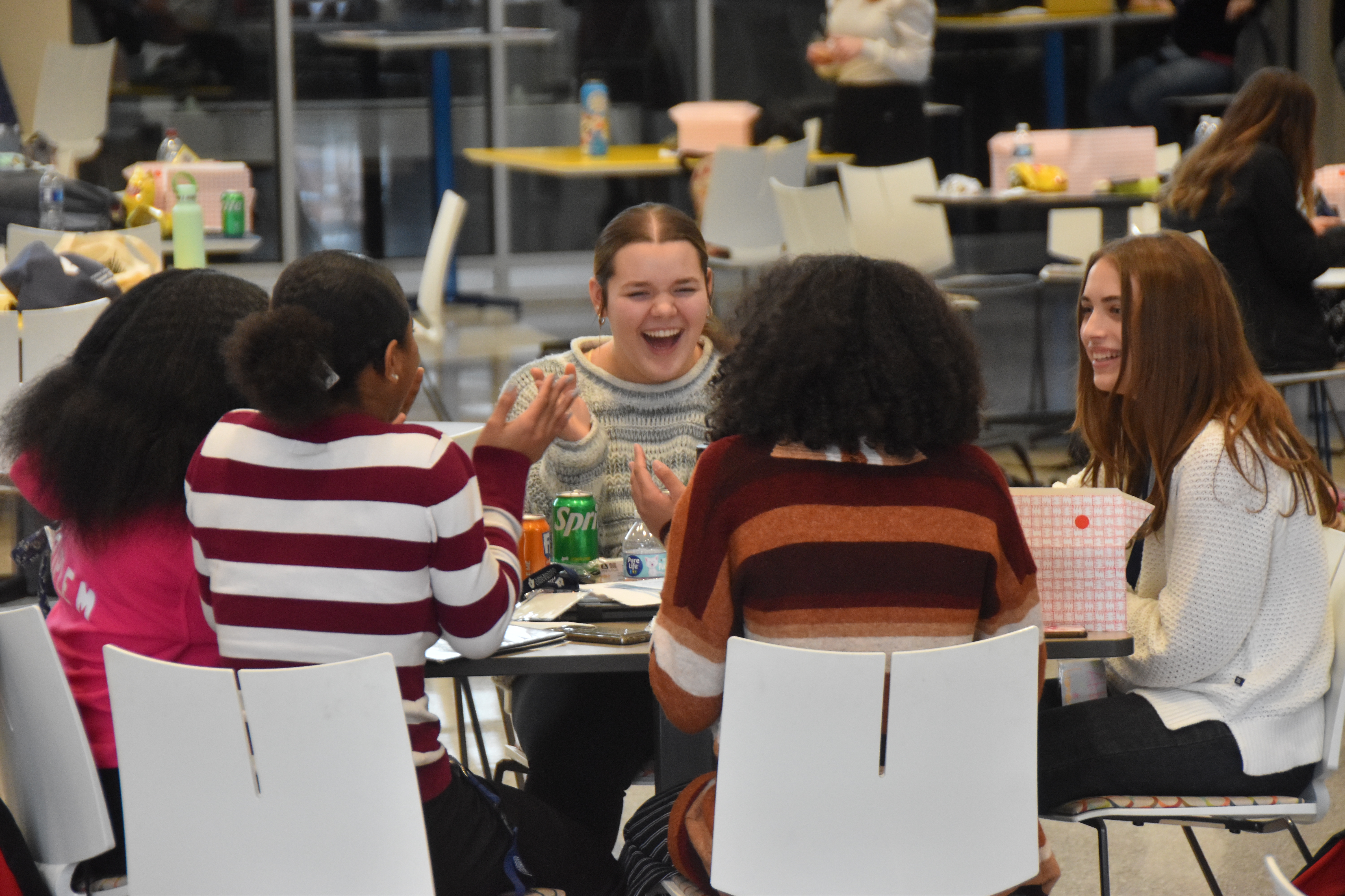 A group of smiling students hanging out while sitting at a table.